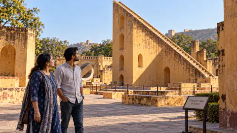 Two visitors explore a historic Indian observatory courtyard beside a masonry sundial